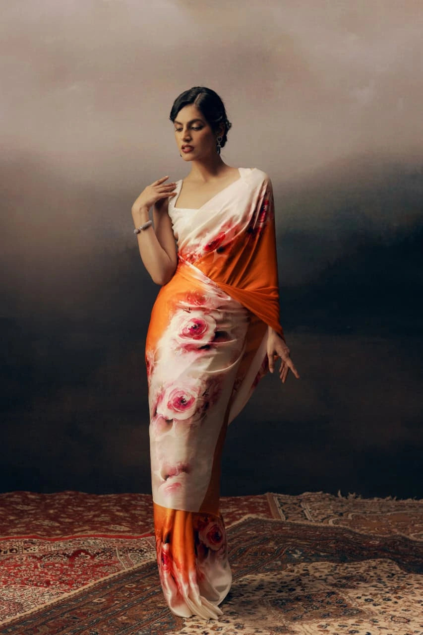 Woman wearing a floral saree with an orange border against a dark background
