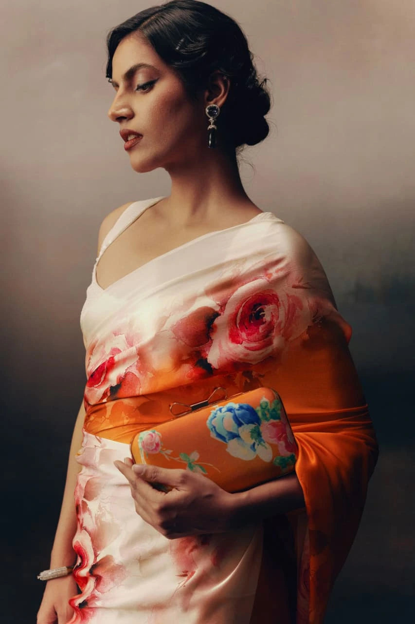 Woman in a floral saree holding a clutch against a dark background