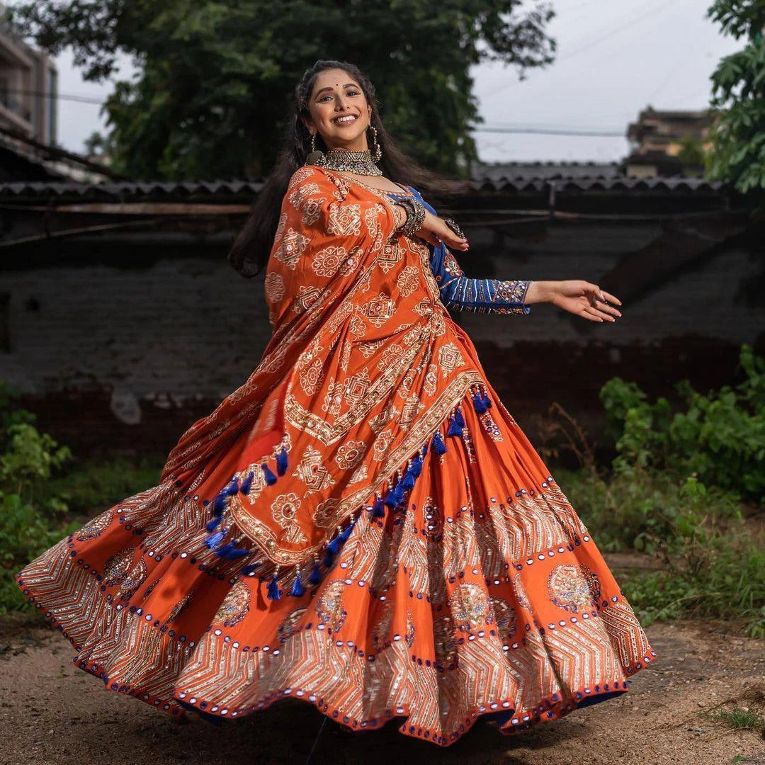 Woman in an orange traditional outfit with blue accents dancing outdoors.