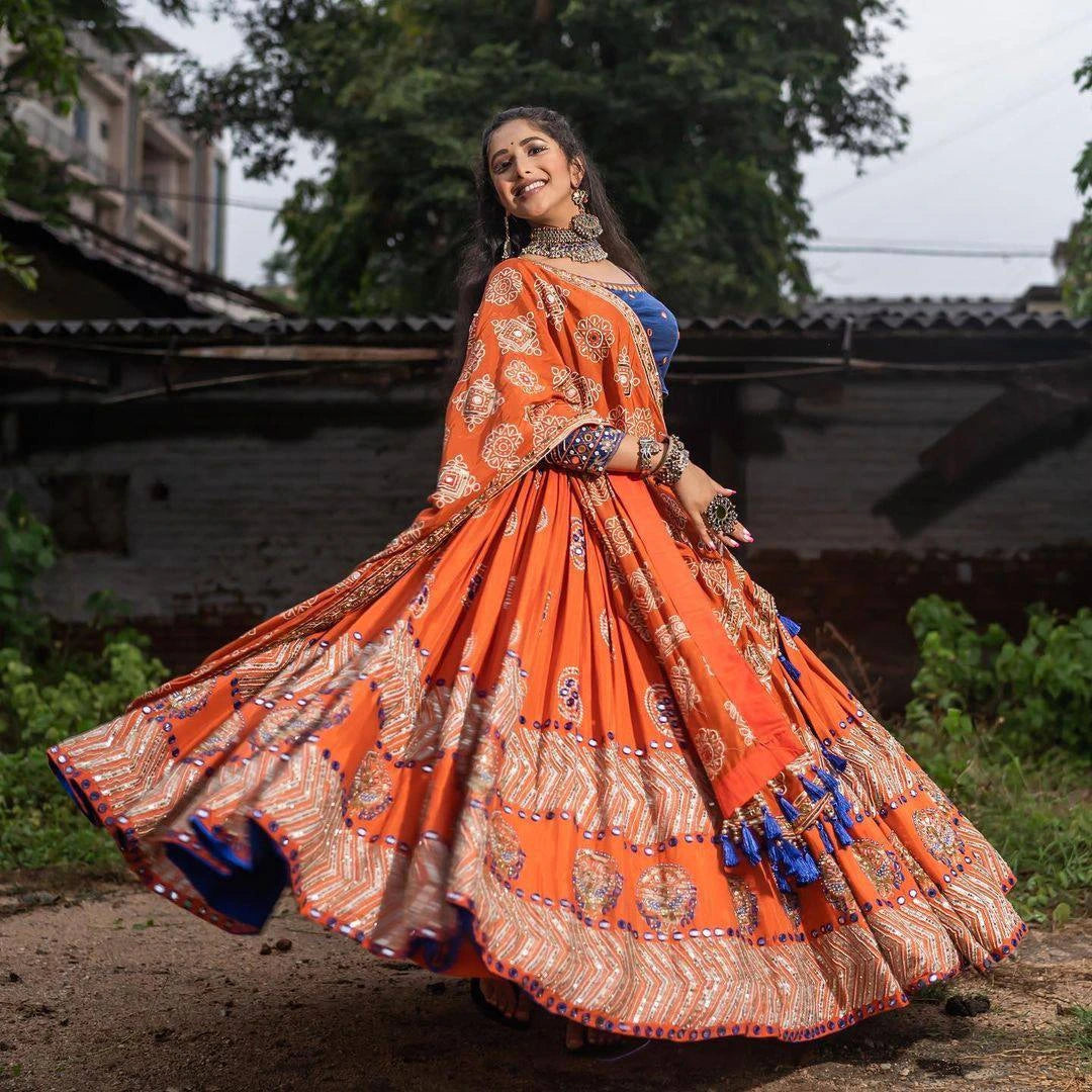 Woman in an orange traditional outfit with a blue blouse, standing outdoors.