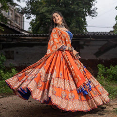 Woman in an orange traditional outfit with a blue blouse, standing outdoors.