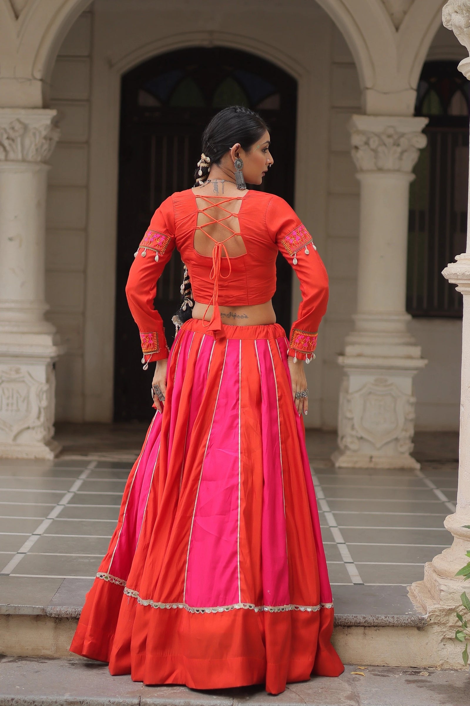 Woman in a red and pink traditional outfit standing in front of an archway.