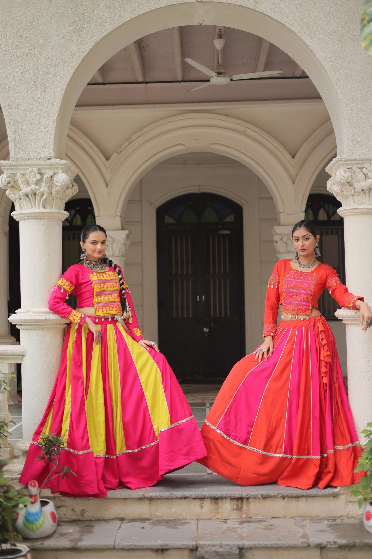 Two women in traditional pink and orange dresses standing under an archway.