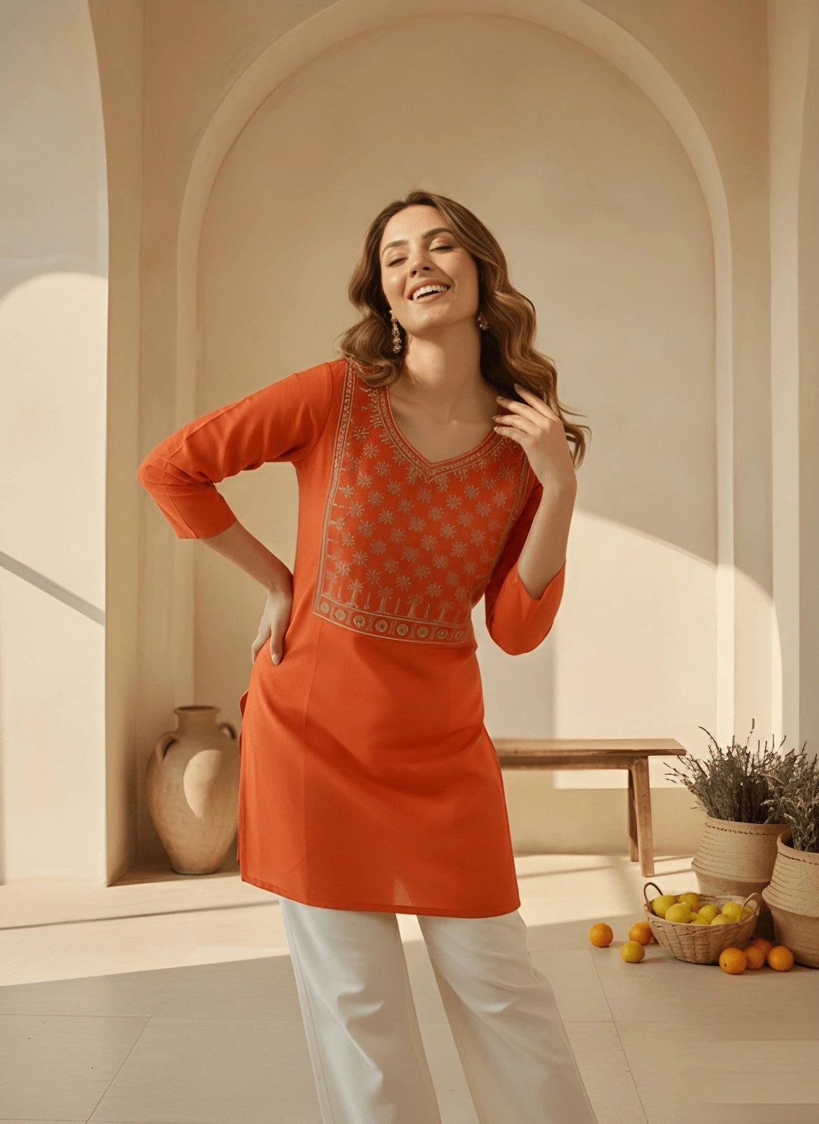 Woman wearing an orange traditional outfit in a sunlit room with plants and fruit.
