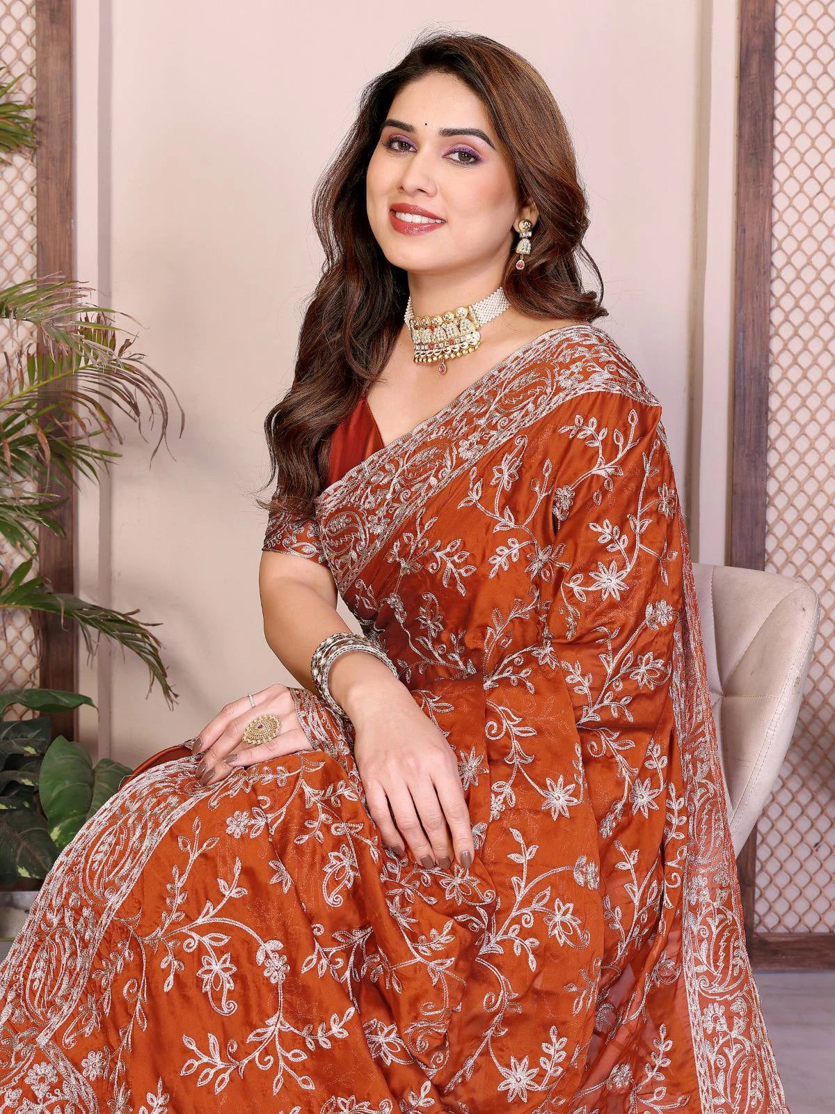 Woman wearing a traditional orange saree with white patterns, sitting indoors.