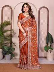 Woman wearing a traditional orange saree with white patterns in a decorative setting with plants.