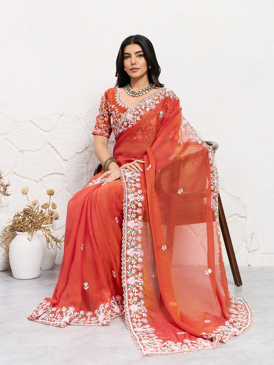 Woman wearing a red saree with white embroidery sitting on a chair.