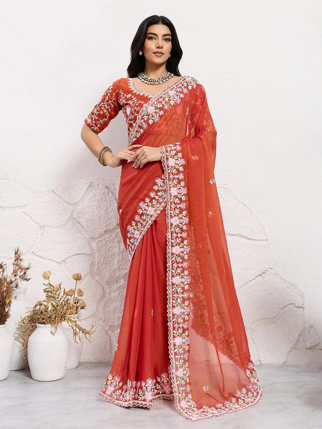 Woman wearing a red saree with white embroidery against a light background