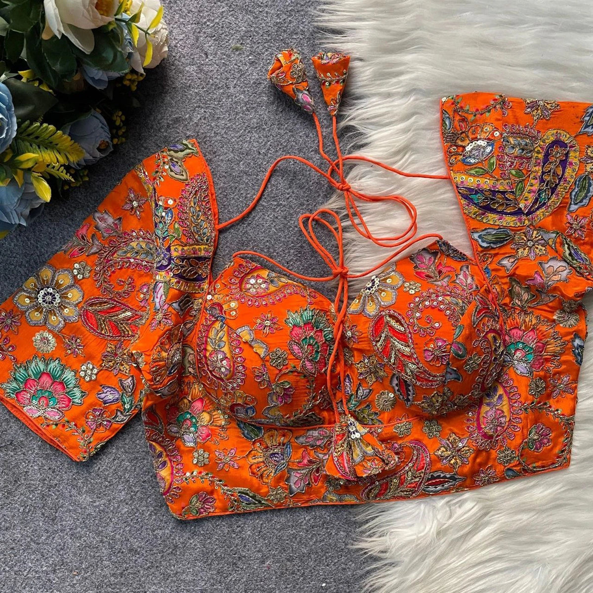 Orange embroidered traditional outfit on a textured surface with flowers in the background