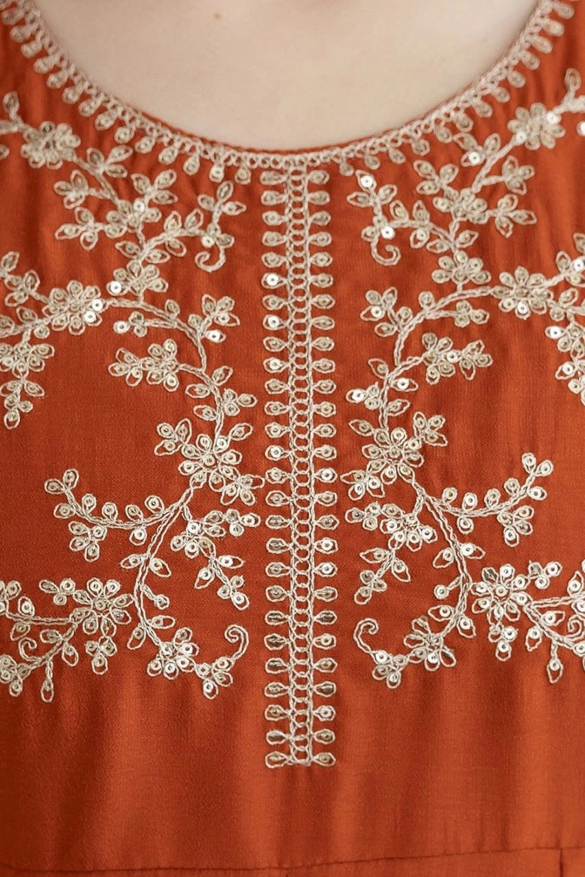 Close-up of a rust-colored fabric with intricate white embroidery