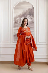 Woman in a red traditional outfit standing in a room with white walls and a decorative mirror.