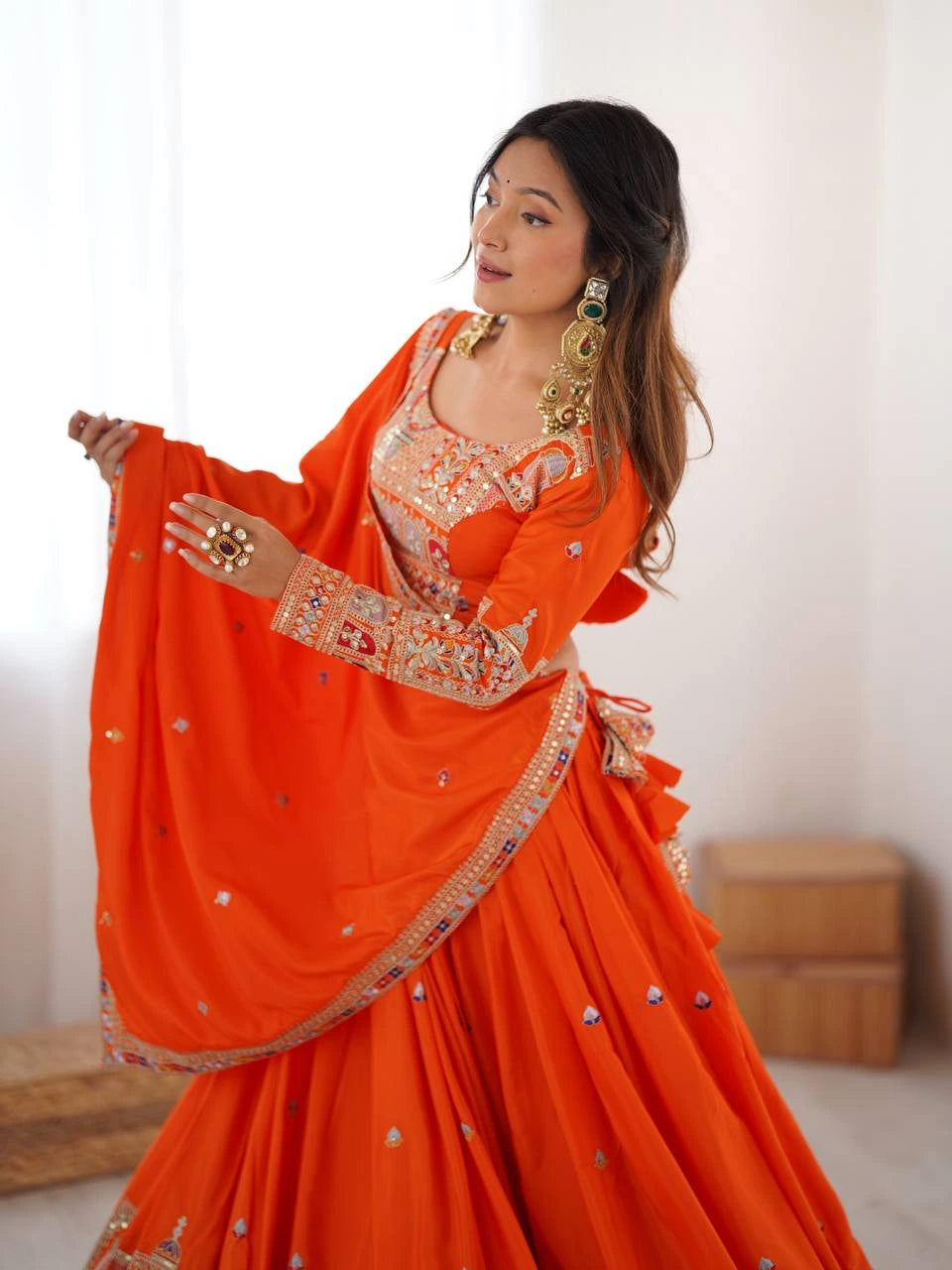 Woman wearing an orange traditional outfit with intricate designs on a plain background