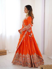 Woman wearing an orange traditional outfit with intricate designs indoors.