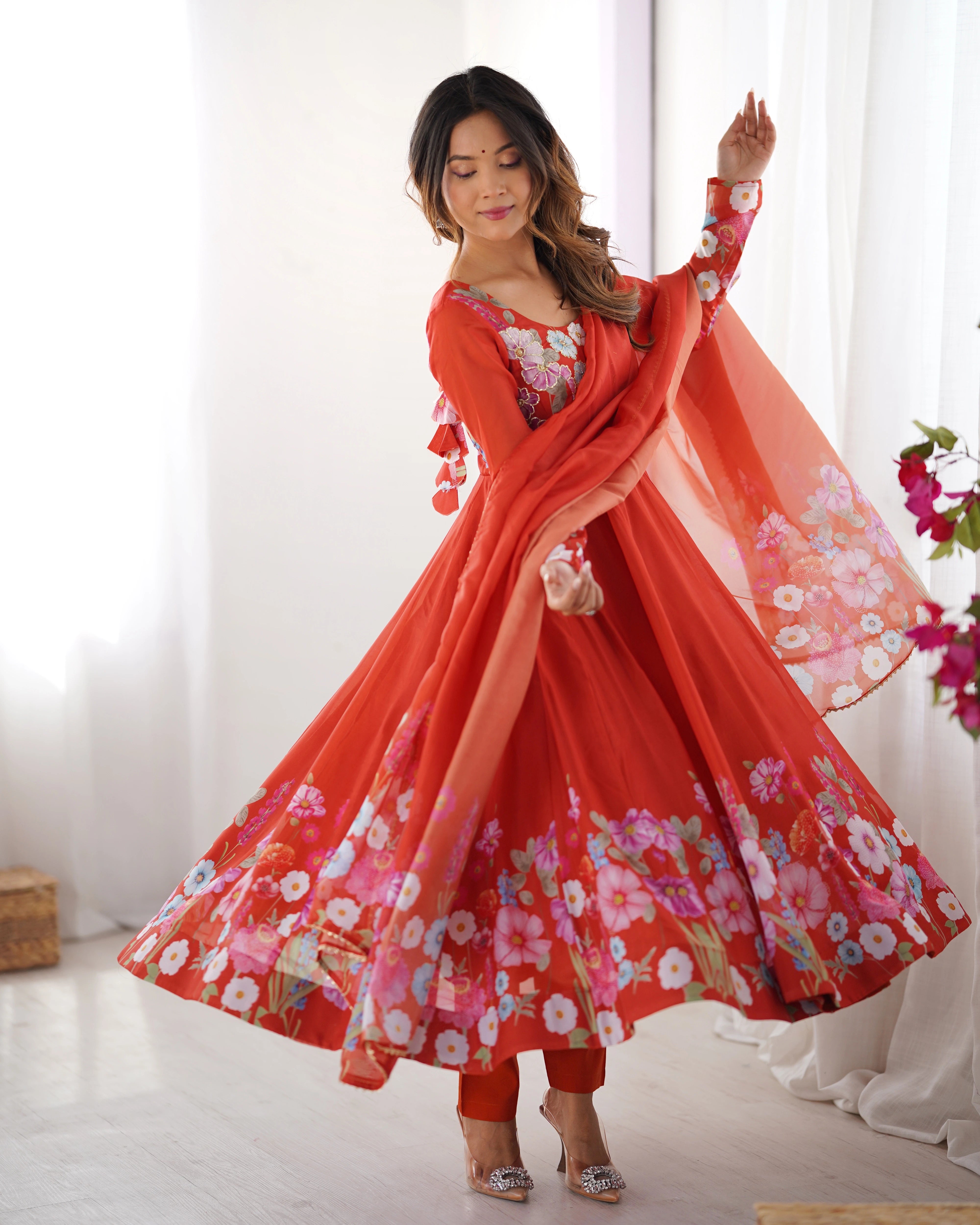 Woman in a red floral dress with a matching dupatta standing in a bright room.
