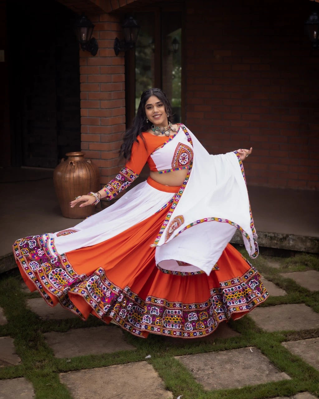 Woman in a traditional orange and white outfit with colorful patterns, standing outdoors.