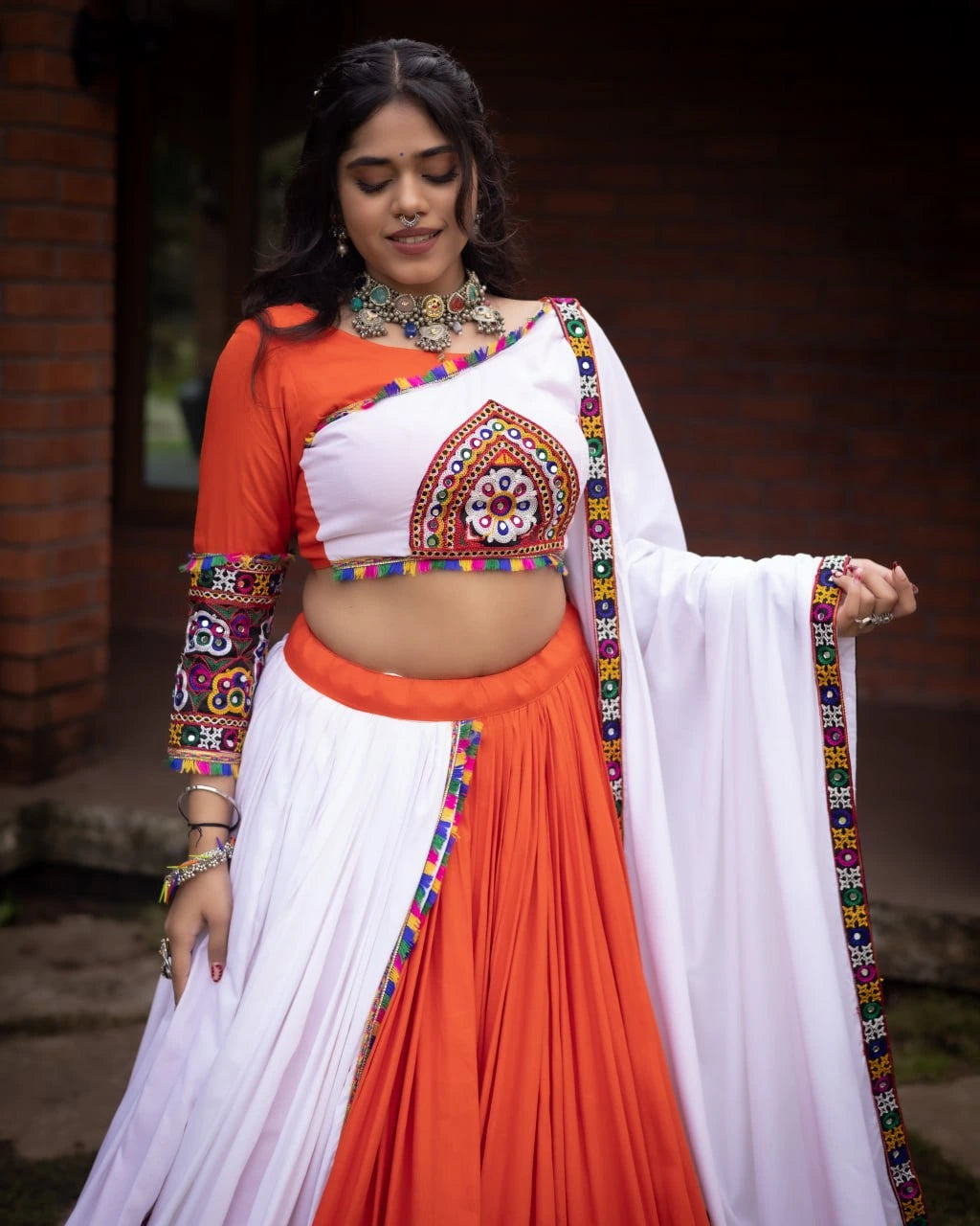 Woman wearing a traditional outfit with orange and white colors, decorated with colorful patterns.