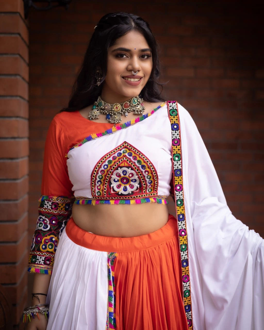 Woman wearing a traditional outfit with colorful patterns against a brick wall.