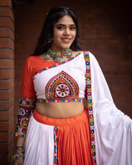 Woman wearing a traditional outfit with colorful patterns against a brick wall.