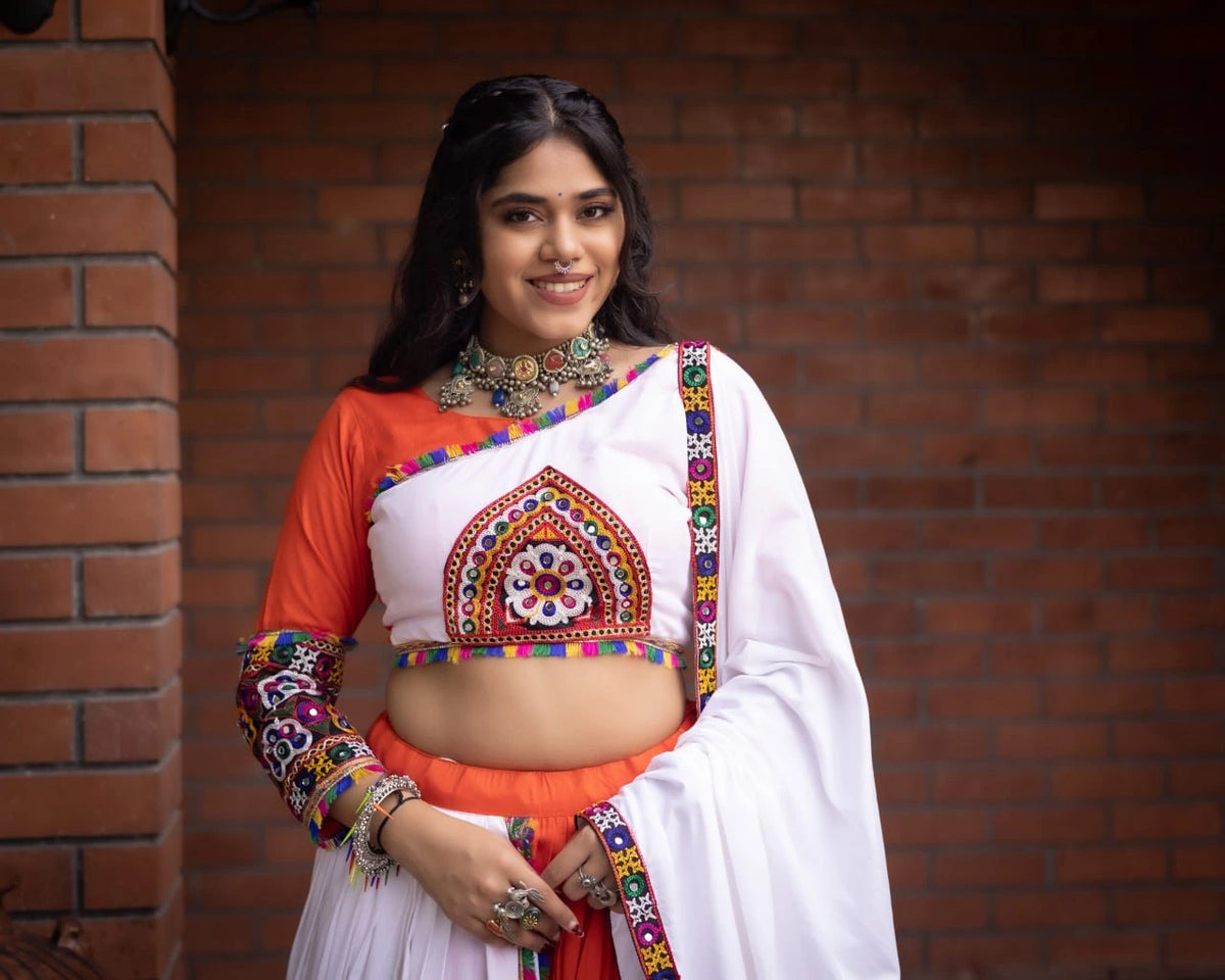 Woman wearing a traditional outfit with colorful patterns against a brick wall.
