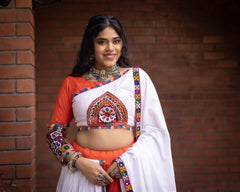 Woman wearing a traditional outfit with colorful patterns against a brick wall.