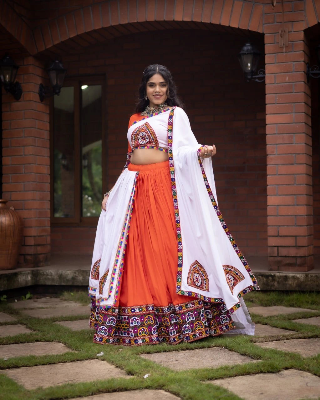 Woman in traditional orange and white outfit standing outdoors with brick wall background