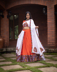 Woman in traditional orange and white outfit standing outdoors with brick wall background