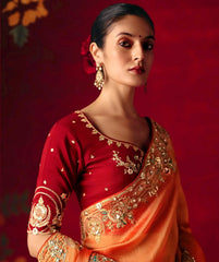 Woman wearing a red and orange saree with gold embroidery against a red background