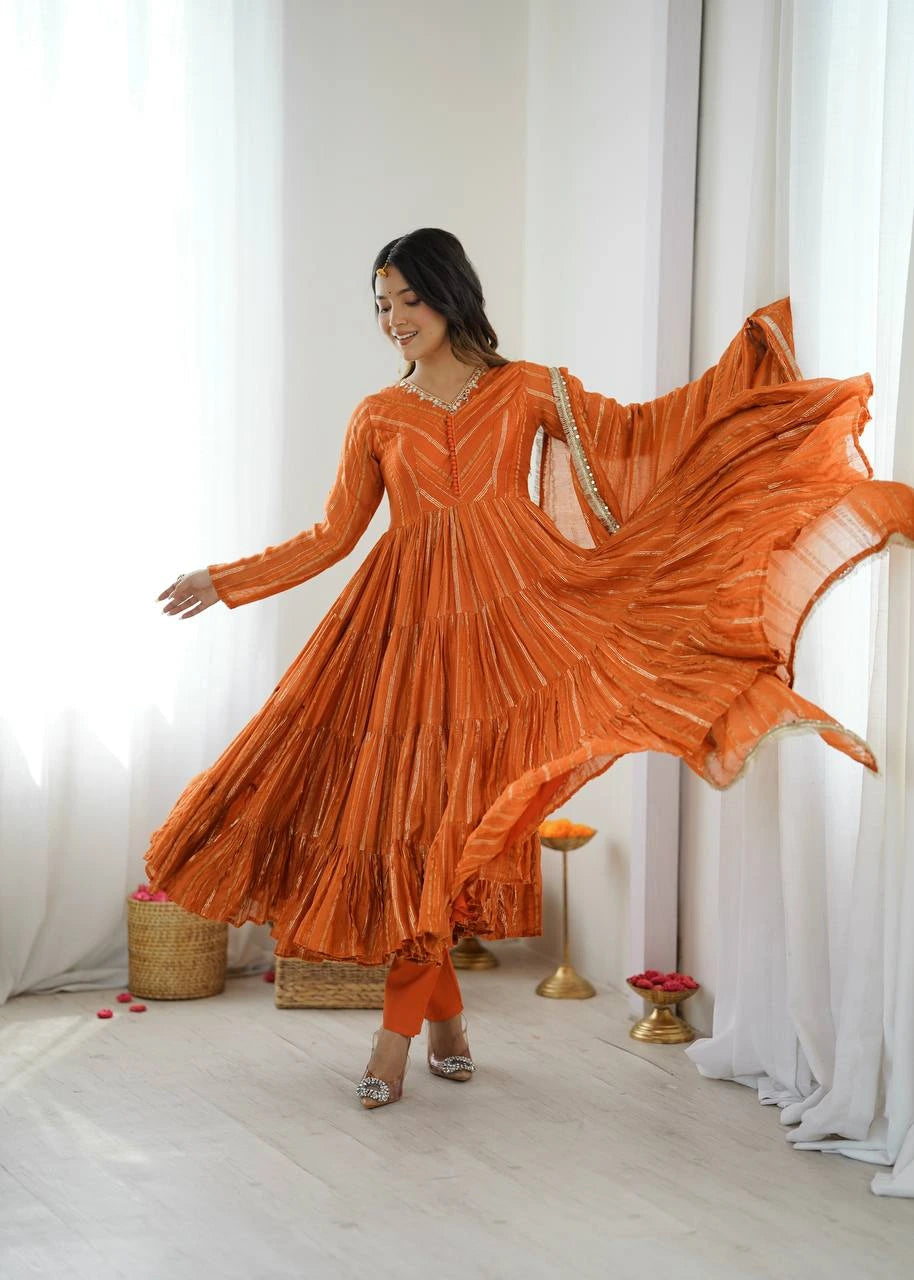 Woman in an orange dress posing in a bright room with white curtains.