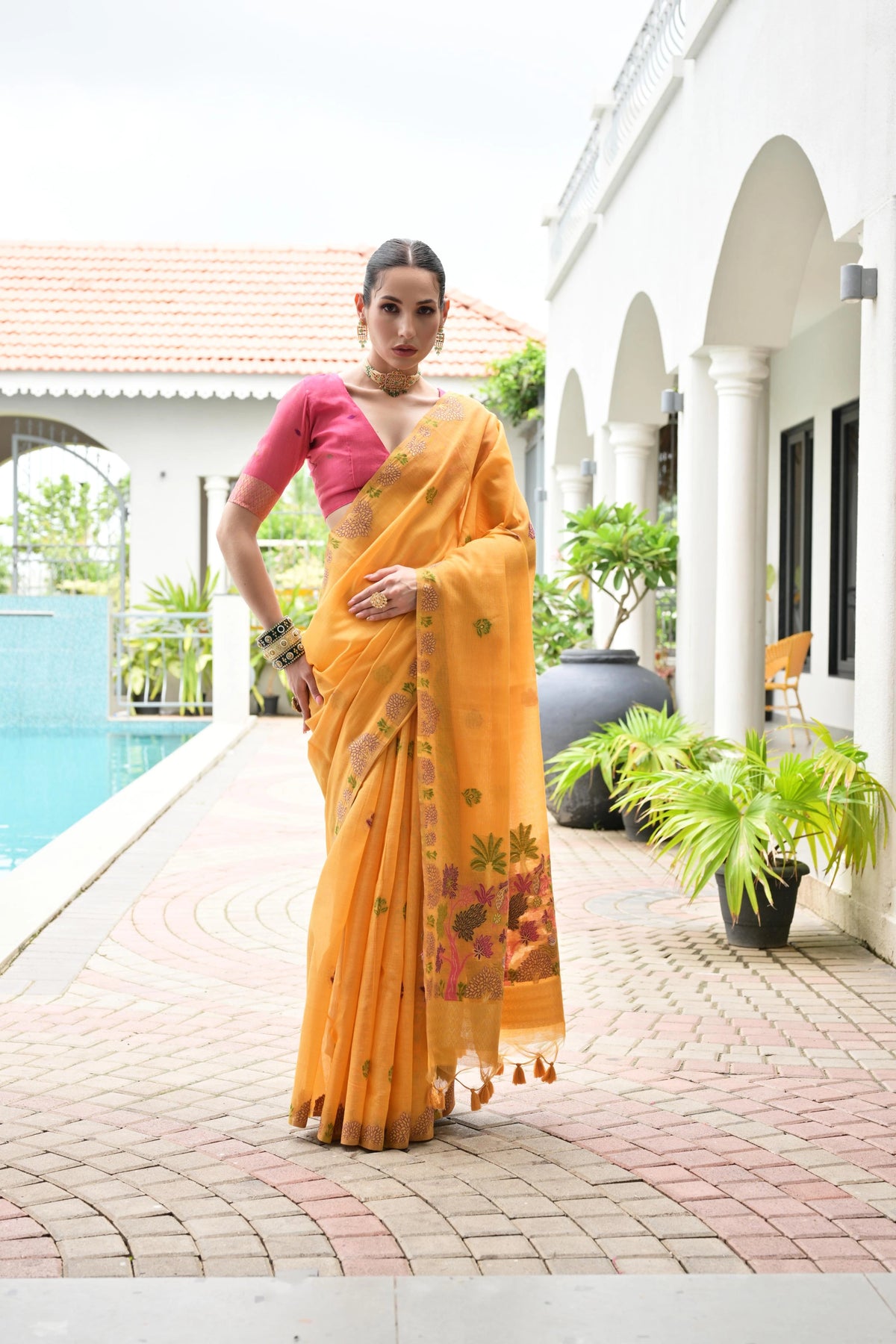 Woman in a yellow saree with a pink blouse standing by a poolside.
