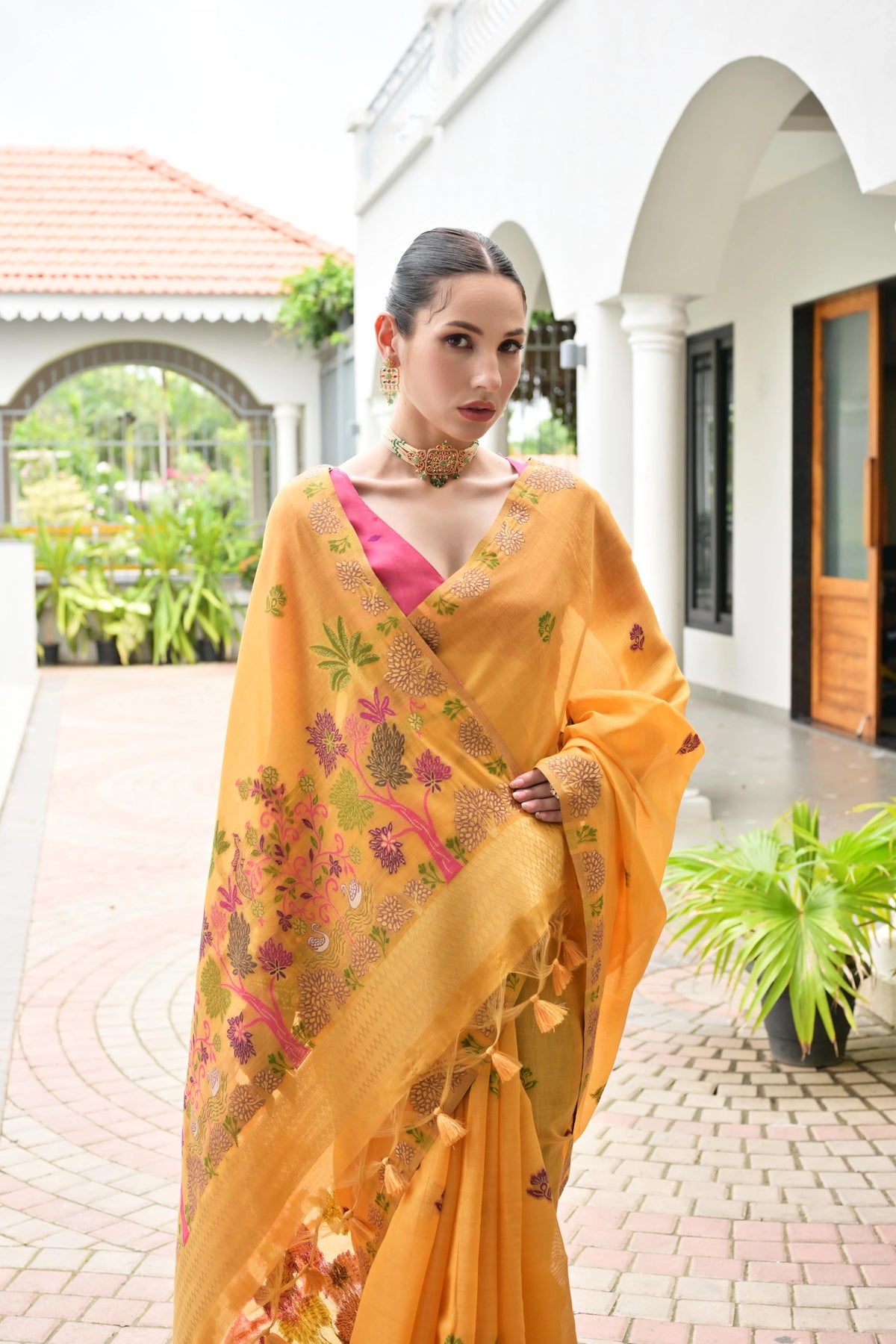 Woman wearing a yellow saree with floral patterns in an outdoor setting.