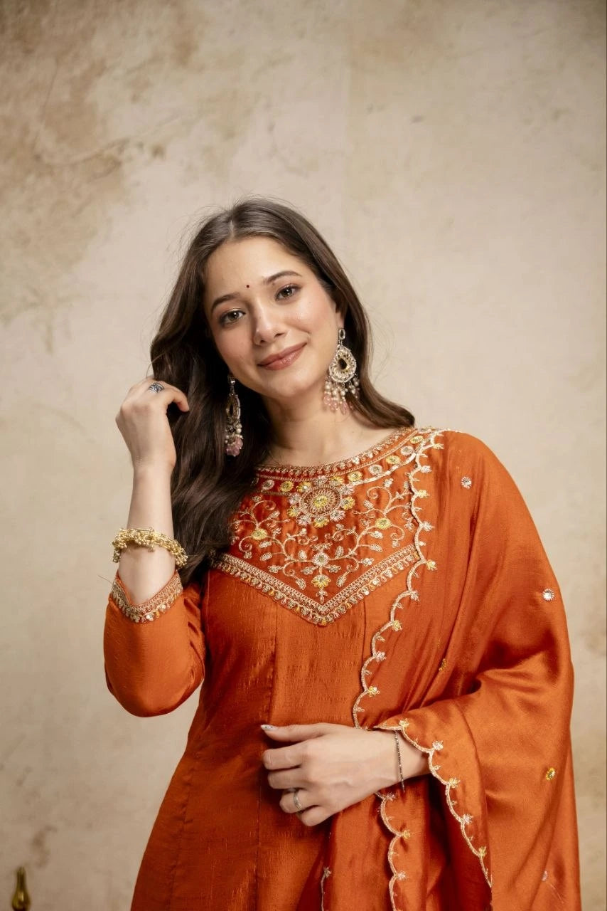 Woman wearing an orange embroidered traditional outfit against a beige background