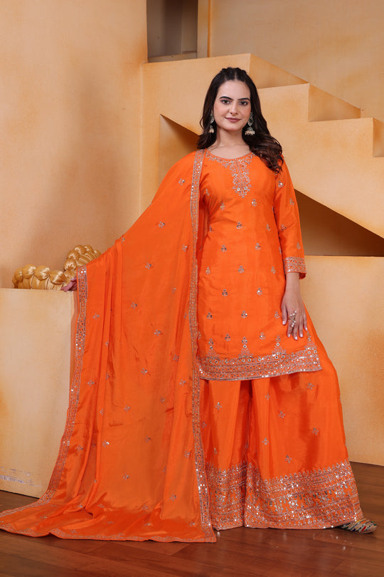 Woman in an orange traditional outfit standing in a room with beige walls and steps.