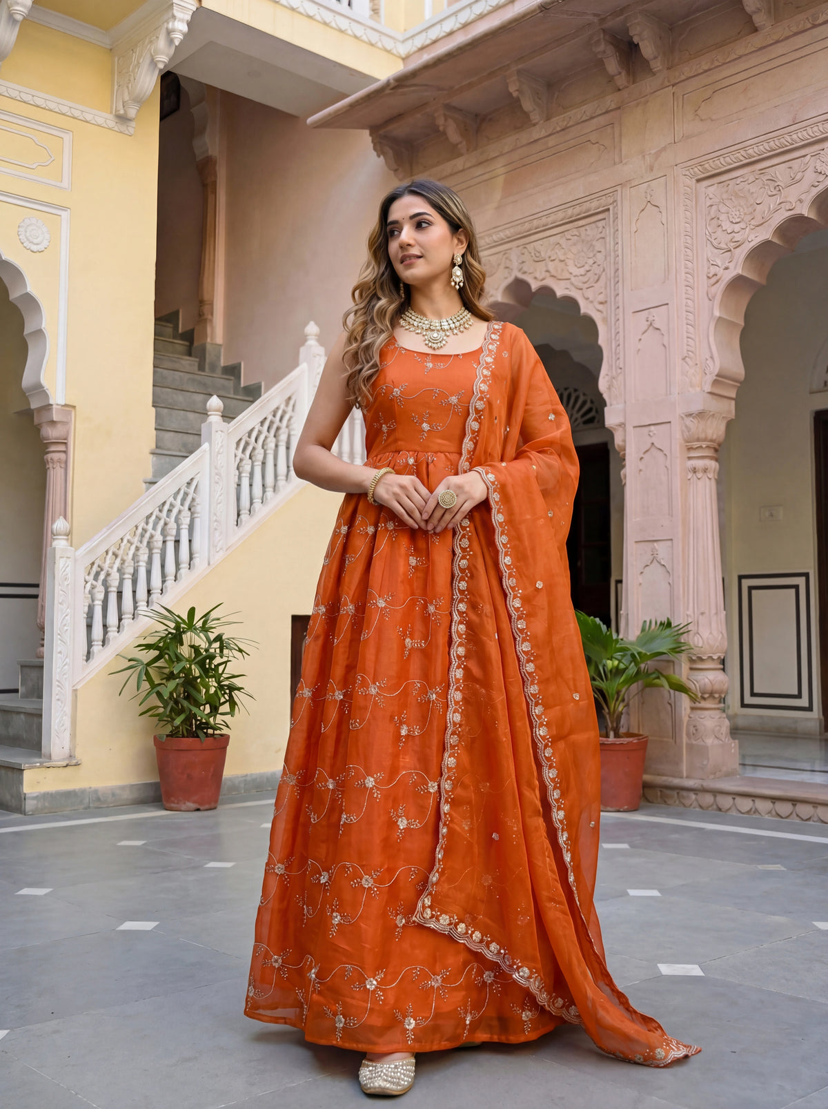 Woman in an orange traditional outfit standing in a decorative courtyard.