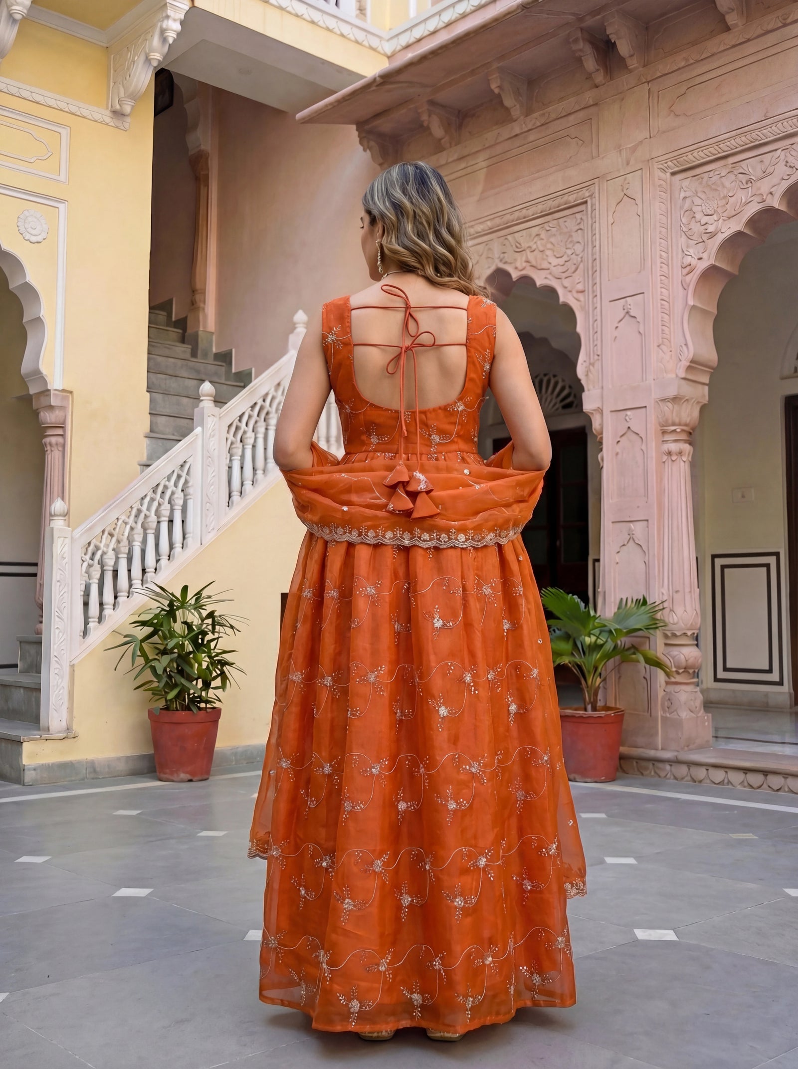 Woman in an orange dress standing in a courtyard with architectural elements.
