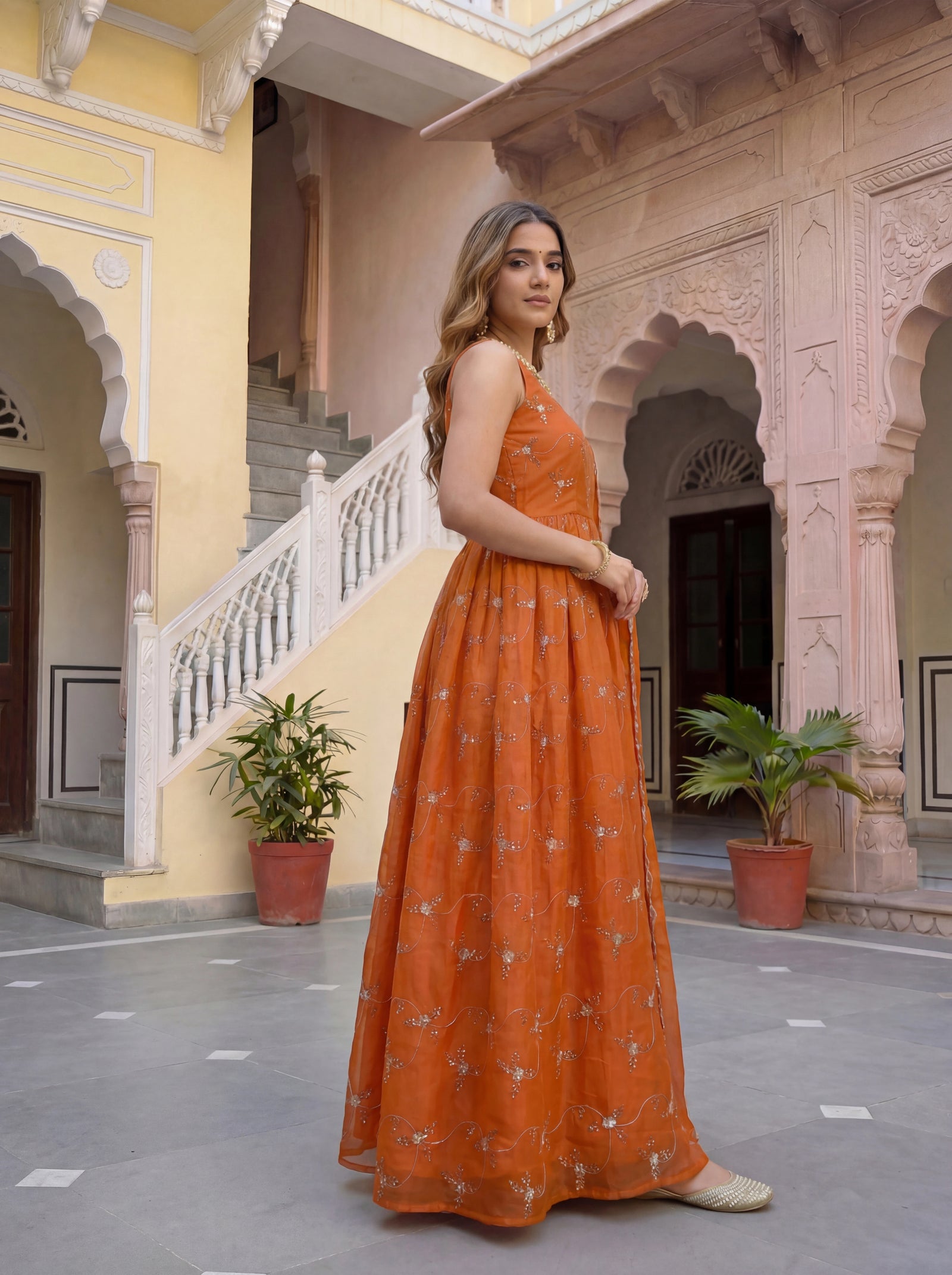Woman in an orange dress standing in a courtyard with architectural elements.