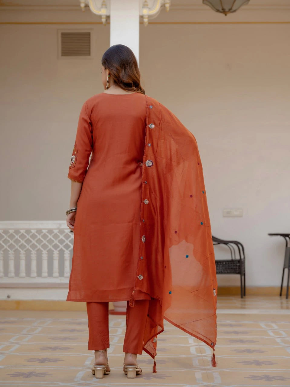 Woman in an orange traditional outfit standing in a room with a neutral color scheme.