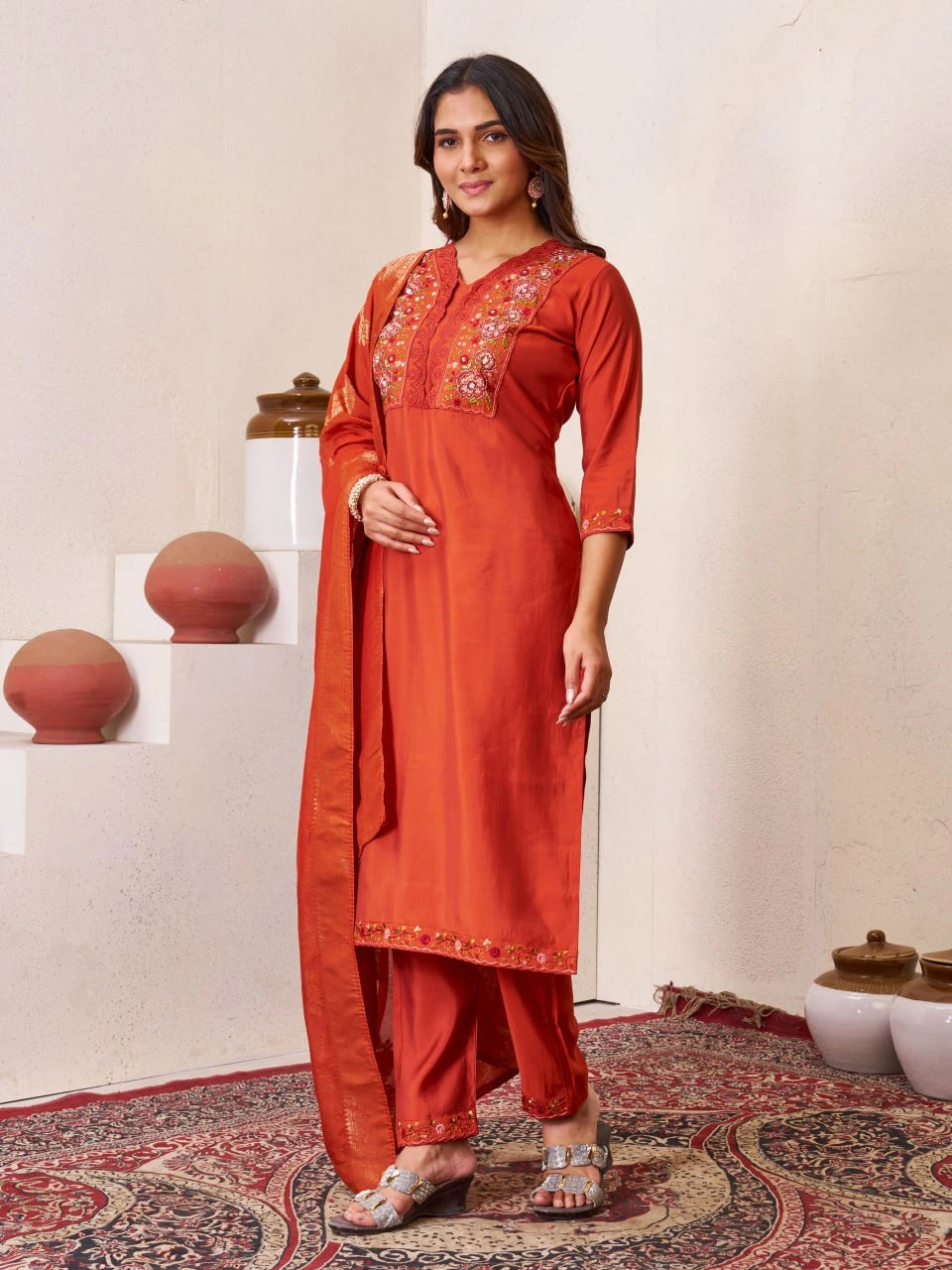 Woman wearing an orange traditional outfit with embroidery in a decorative room.
