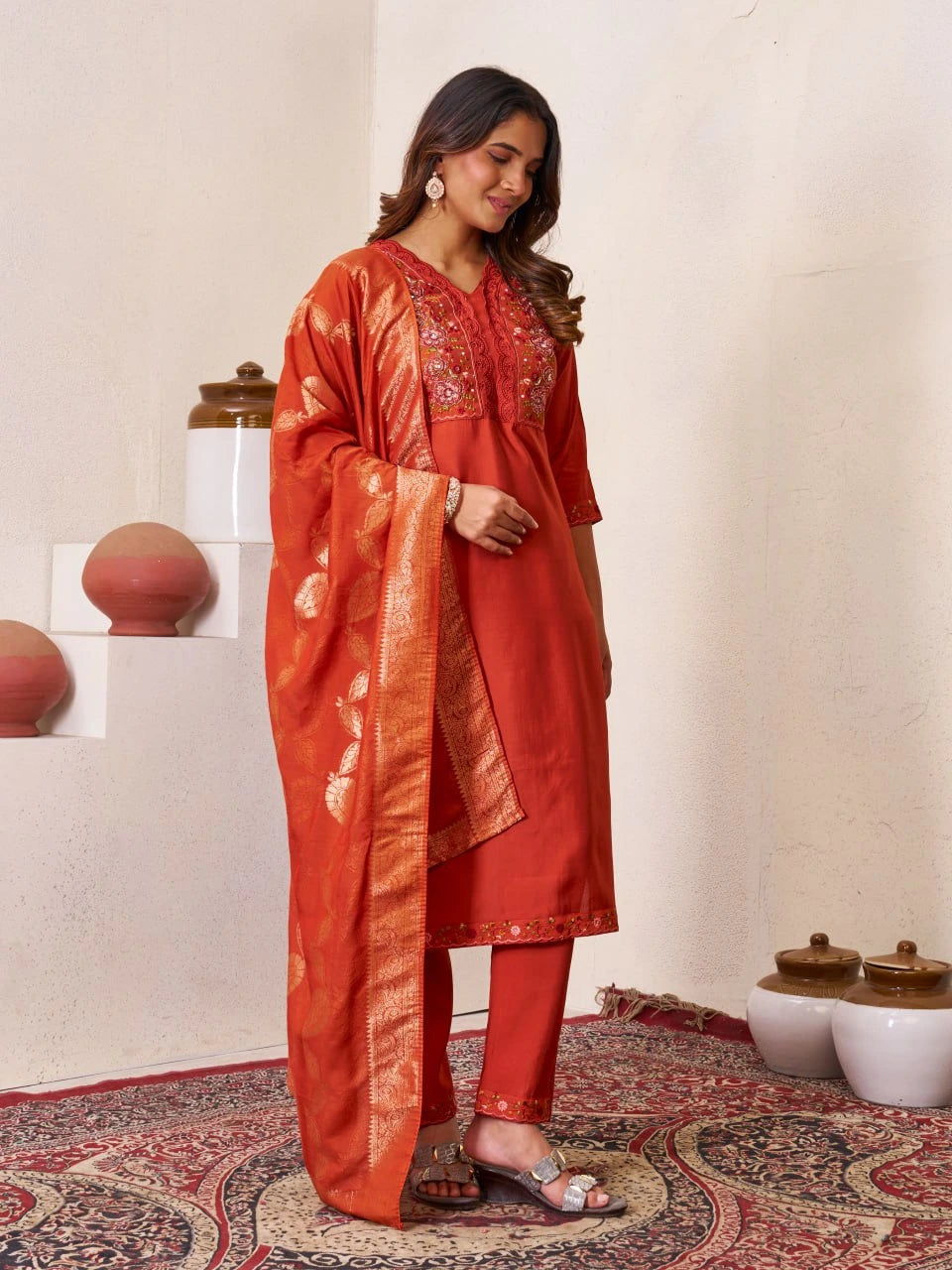 Woman in a traditional red outfit standing in a decorative room with white walls and patterned rug.