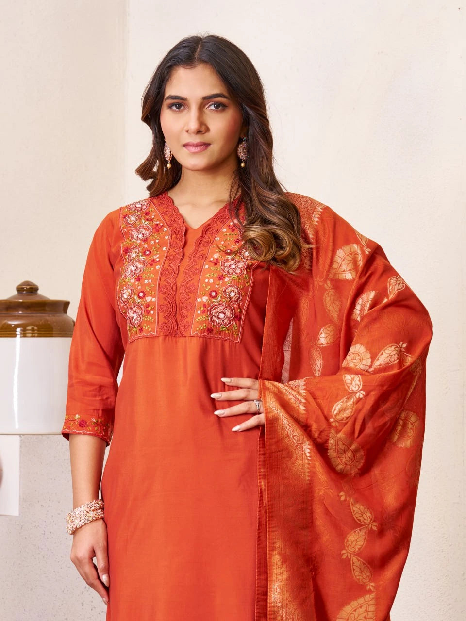 Woman wearing an orange embroidered traditional outfit against a neutral background