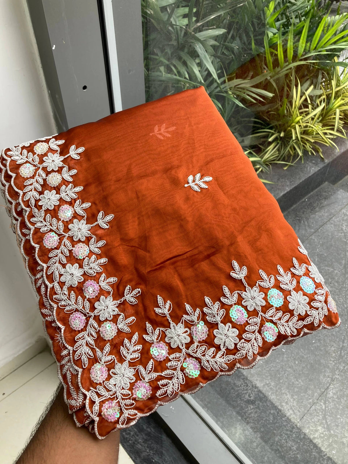Orange pillow with white floral embroidery on a window sill.