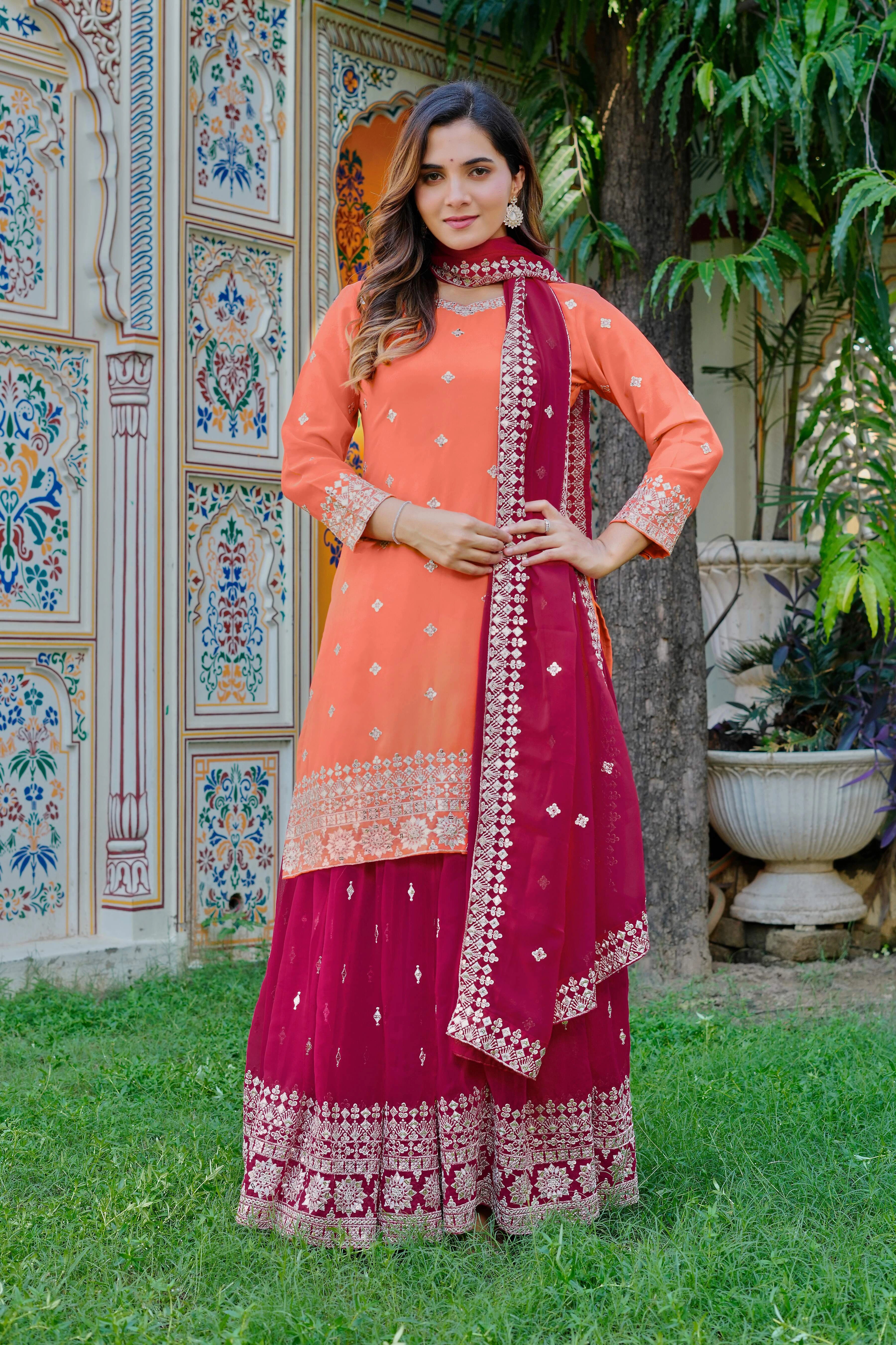 Woman in traditional pink and orange outfit with embroidered details standing in a garden.