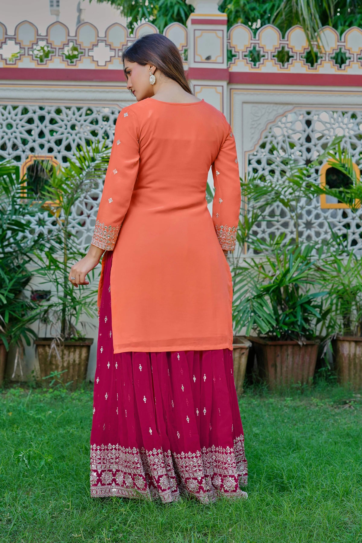 Woman wearing an orange top and pink skirt with a patterned border, standing outdoors.