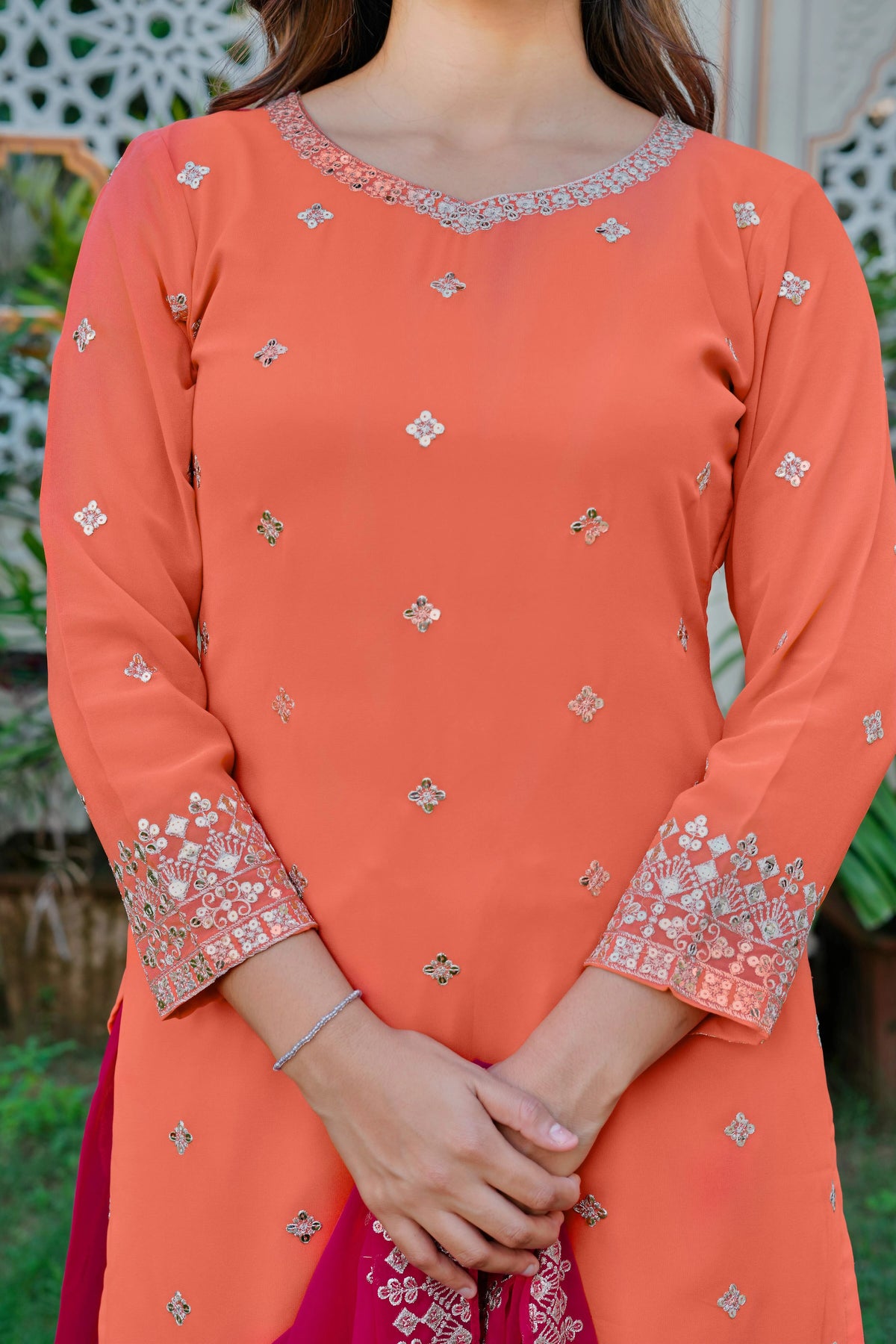 Person wearing an orange embroidered traditional outfit with a blurred green background