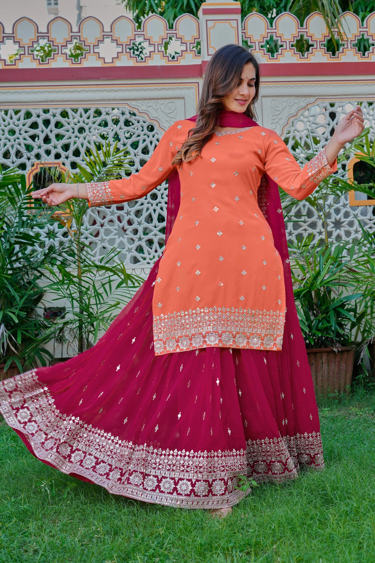 Woman in an orange and pink traditional outfit standing in a garden.