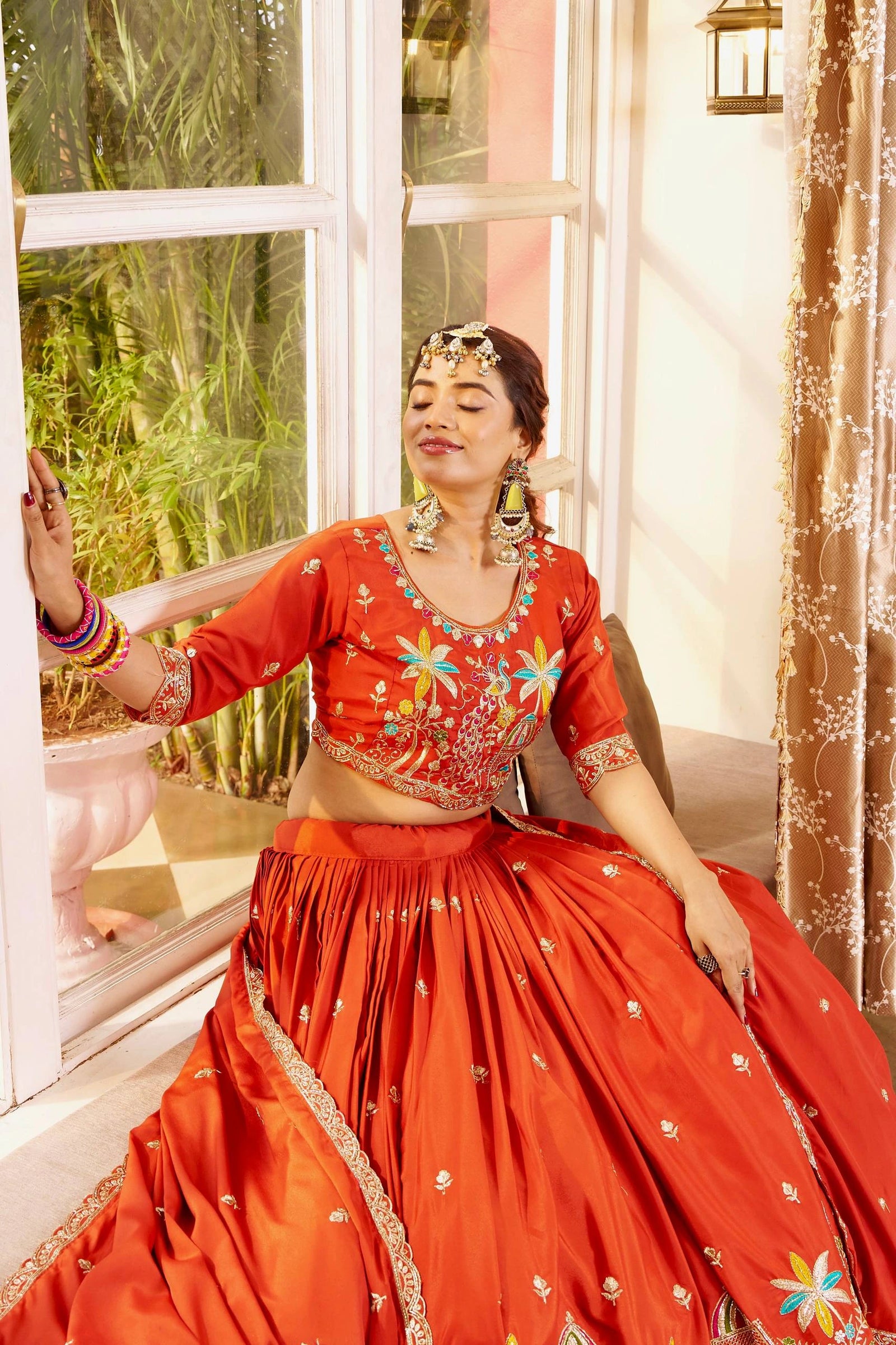 Woman in a red traditional outfit with floral patterns sitting by a window.