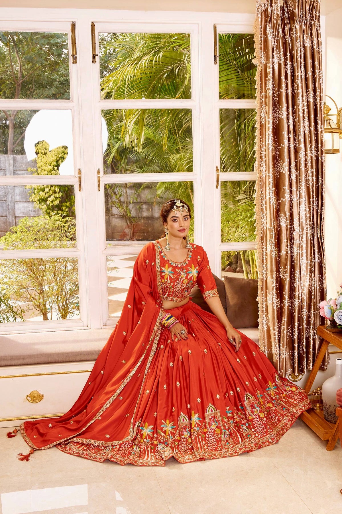Woman in a red traditional outfit sitting by a window with greenery outside