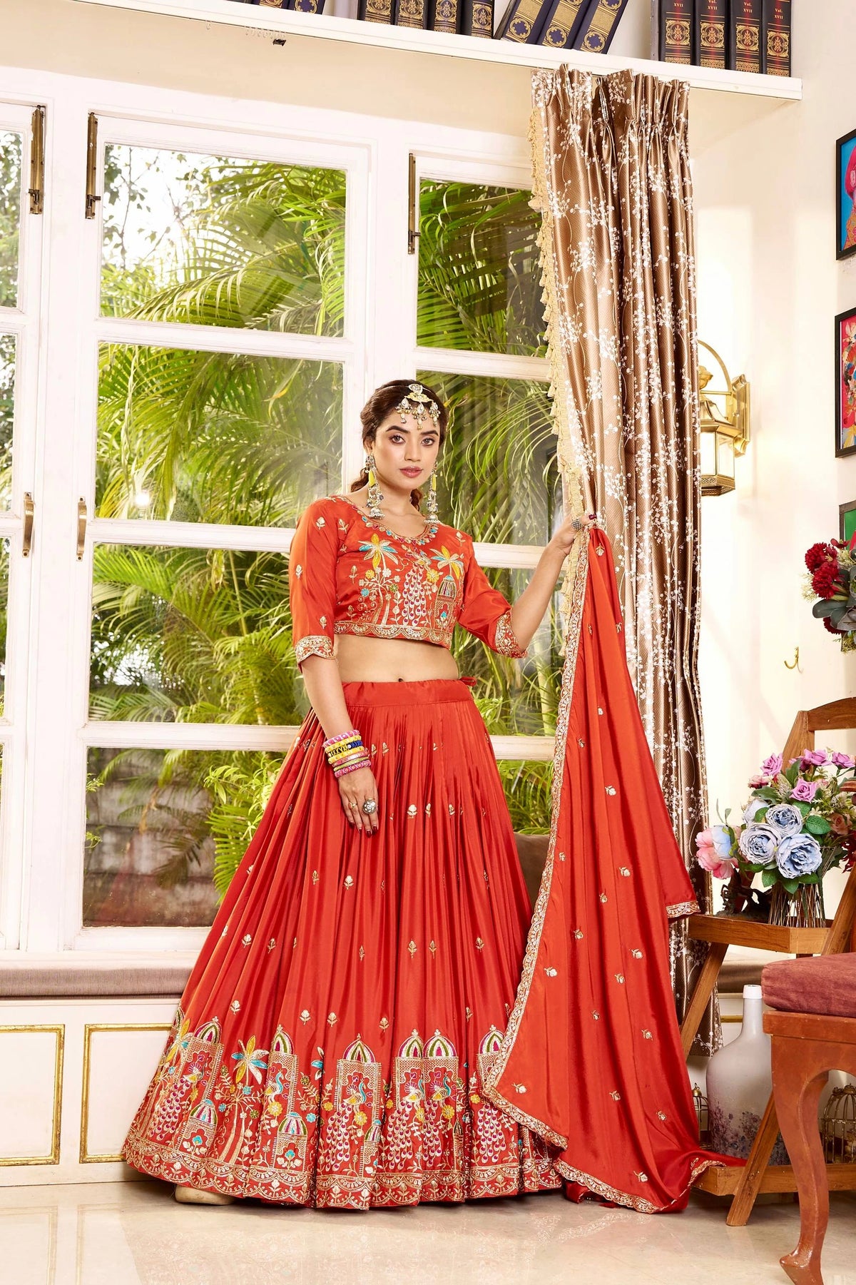 Woman in a red traditional outfit standing in a room with a window and decor.
