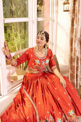 Woman in a red traditional outfit with floral patterns sitting by a window.