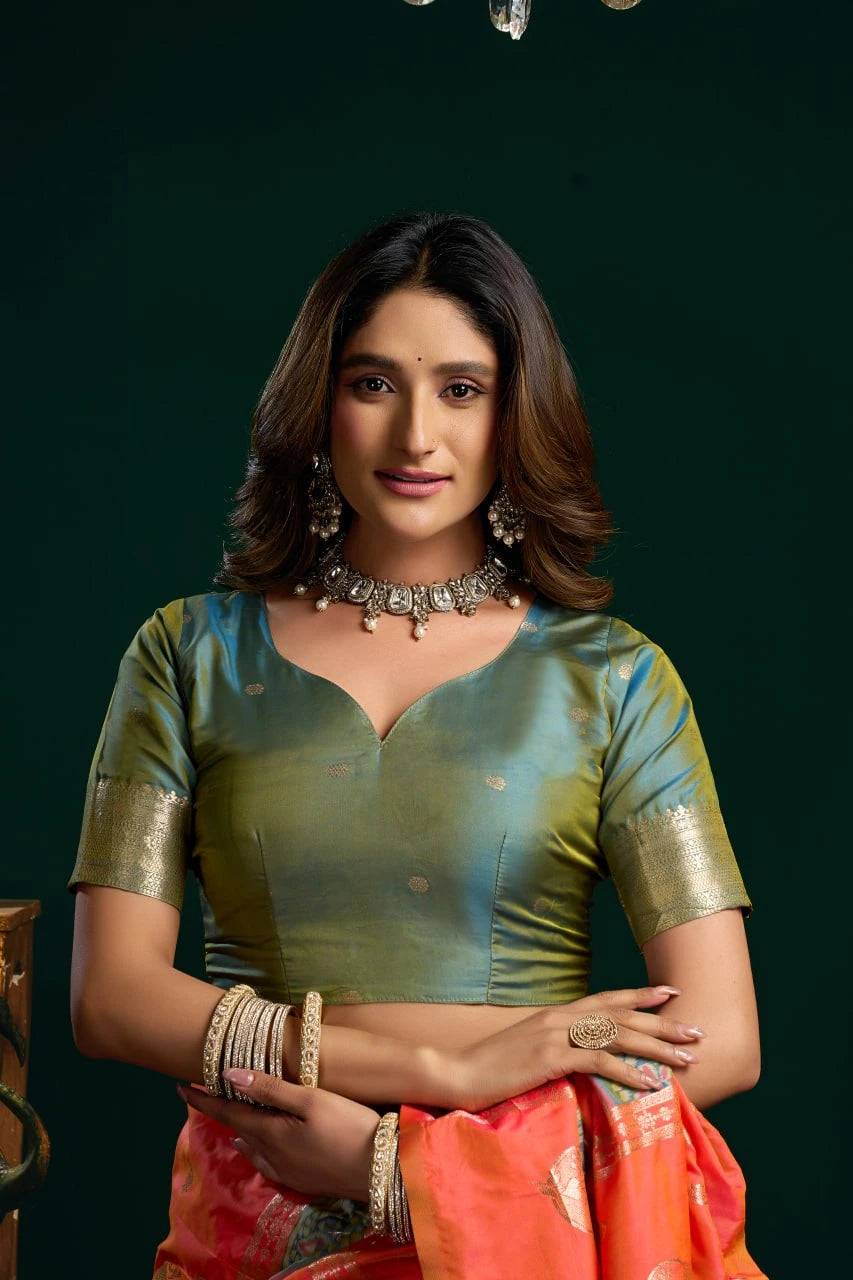 Woman wearing a green blouse and orange saree with jewelry against a dark background