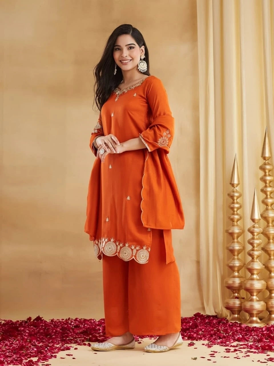 Woman wearing an orange traditional outfit with gold details against a beige background.